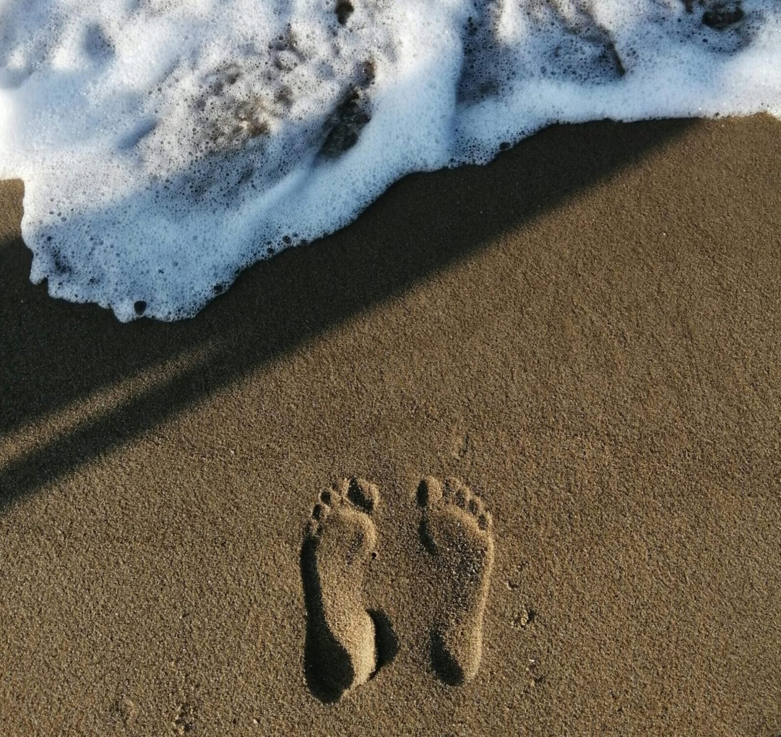 Footprints on a sandy beach with waves approaching, captured from above.